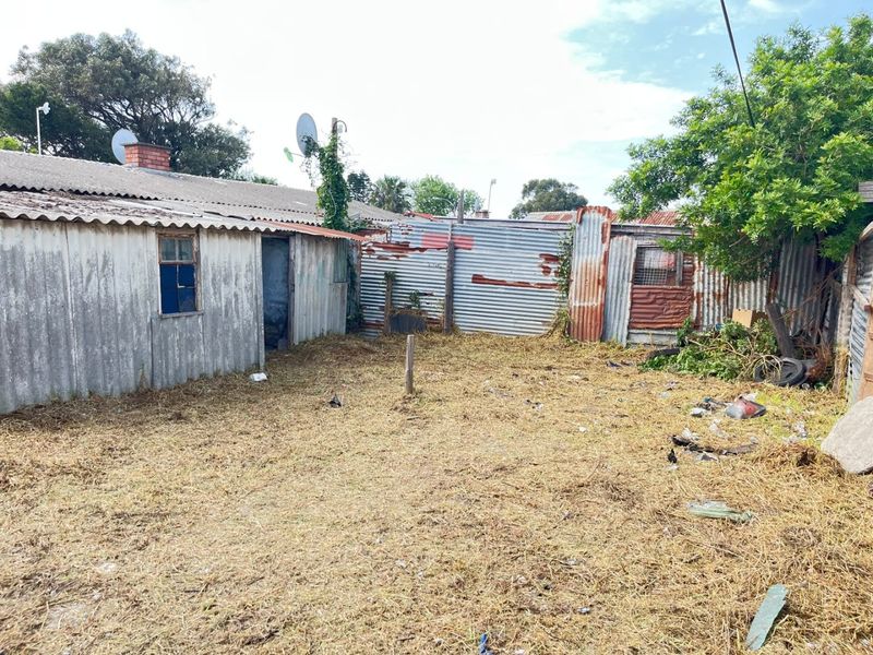Rear exterior view of the property featuring corrugated iron structures and fencing in a state of significant disrepair.