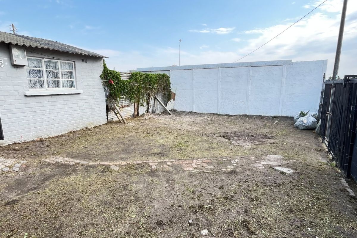 A rear yard area featuring a precast concrete boundary wall, metal security gate, and an unlandscaped garden space requiring significant maintenance and improvement.