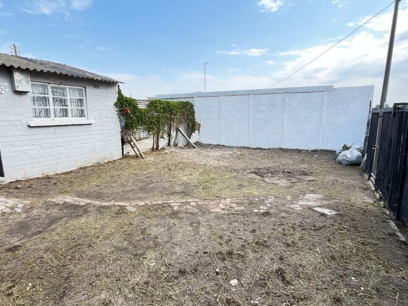 A rear yard area featuring a precast concrete boundary wall, metal security gate, and an unlandscaped garden space requiring significant maintenance and improvement.