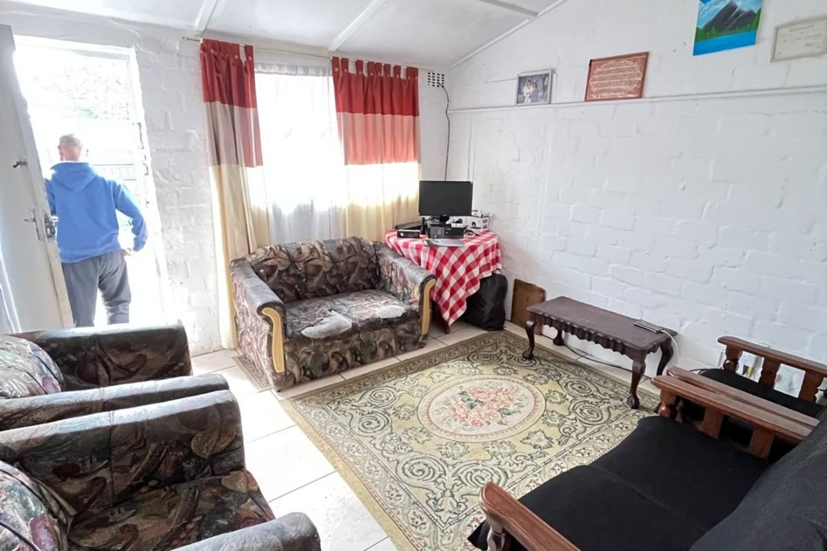 A living room featuring tiled flooring, painted brick walls, and an exposed beam ceiling, with direct access to the exterior.