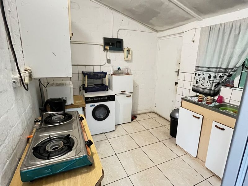 A compact kitchen featuring tiled flooring, a gas hob, and basic cabinetry. The space requires cosmetic updates and maintenance to improve its overall condition.
