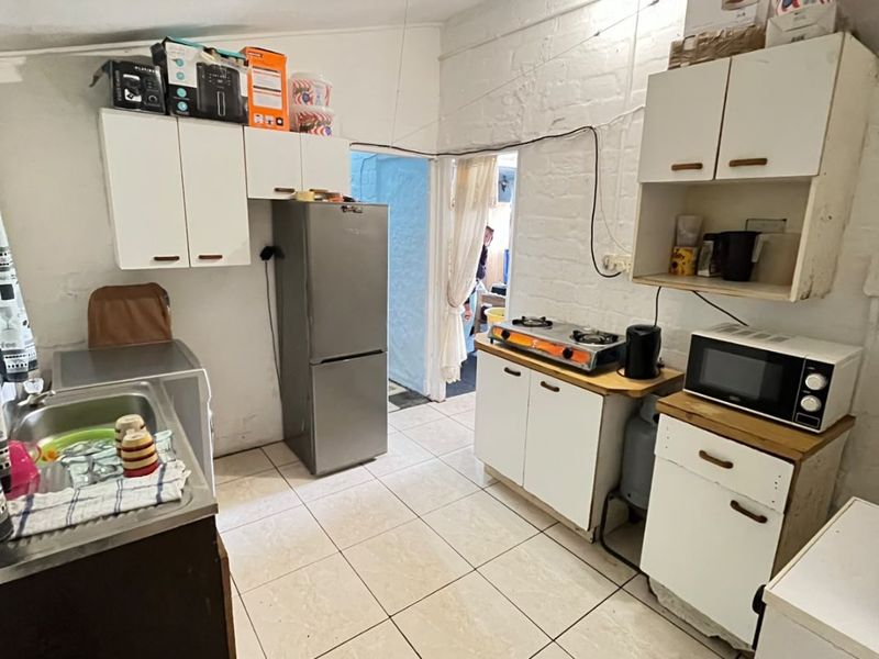 A functional kitchen space featuring tiled flooring, built-in cabinetry, a stainless steel sink, and a gas cooktop, requiring cosmetic updates.