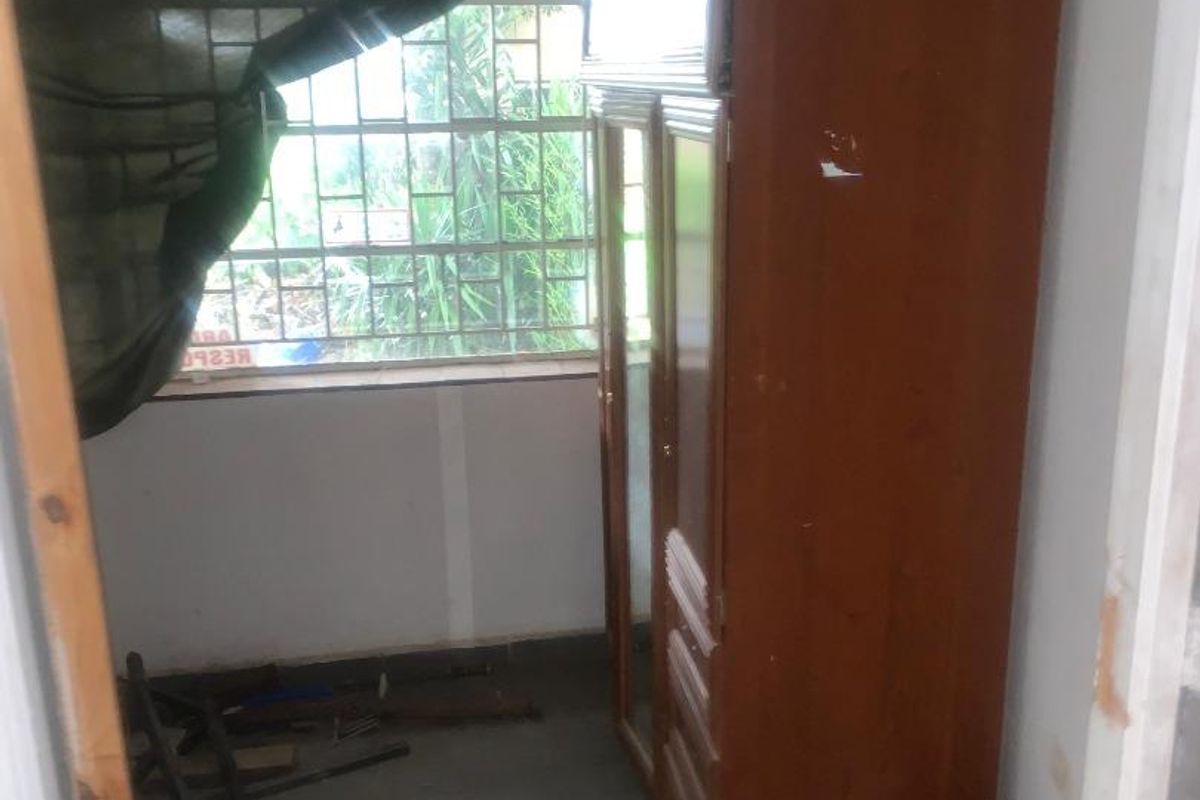 A small bedroom featuring tiled flooring and security bars on the window, currently in need of cosmetic repairs and maintenance.