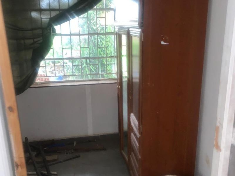 A small bedroom featuring tiled flooring and security bars on the window, currently in need of cosmetic repairs and maintenance.
