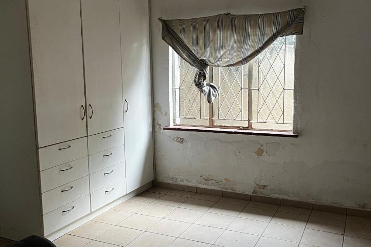 A bedroom featuring built-in cupboards, tiled flooring, and a decorative ceiling, currently requiring wall repairs and cosmetic updates.
