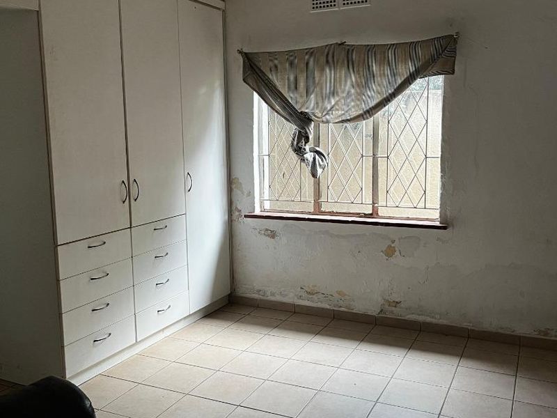 A bedroom featuring built-in cupboards, tiled flooring, and a decorative ceiling, currently requiring wall repairs and cosmetic updates.