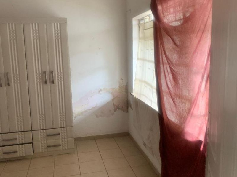 A bedroom featuring tiled flooring, a built-in wardrobe, and decorative ceiling details, currently showing significant signs of wall water damage and staining.