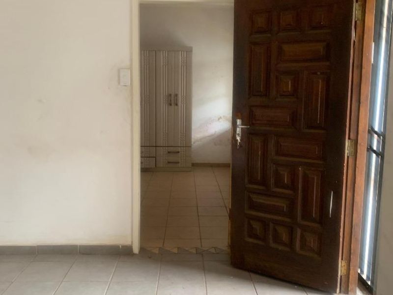 A vacant hallway featuring tiled flooring and a solid timber door, leading into an adjacent room with built-in cabinetry.
