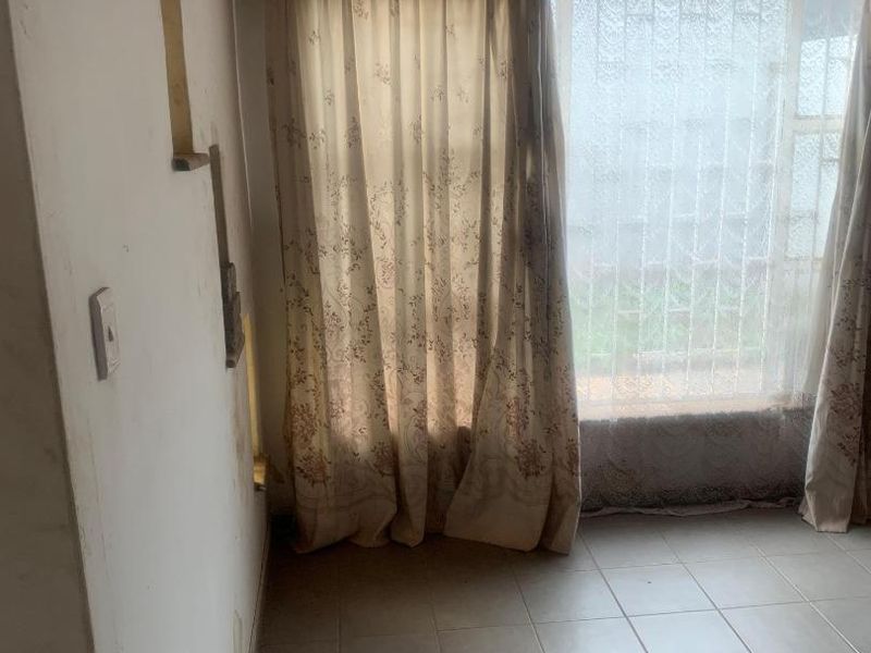 An empty bedroom featuring tiled flooring, a timber pelmet, and security bars on the window, requiring cosmetic updates to the wall finishes.
