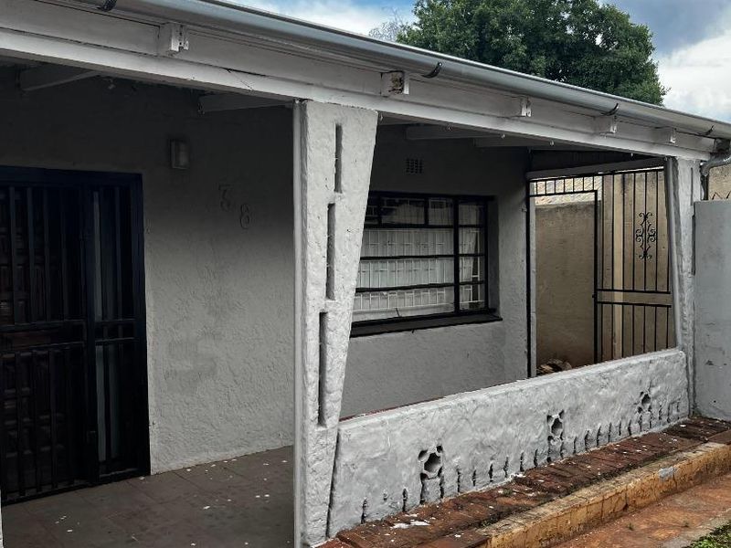 Front exterior view of the house featuring a covered patio area with security gates, security bars, and paved entrance.