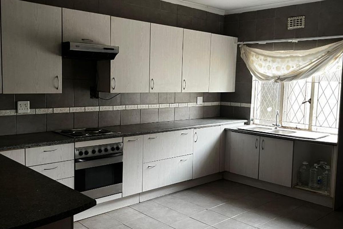 A functional kitchen featuring built-in cabinetry, dark tiled backsplash, integrated oven and hob, and tiled flooring throughout.