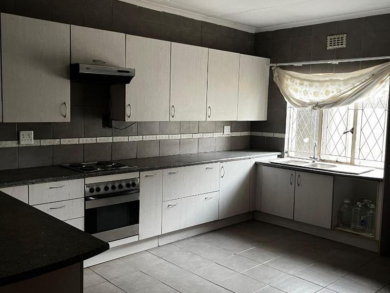 A functional kitchen featuring built-in cabinetry, dark tiled backsplash, integrated oven and hob, and tiled flooring throughout.
