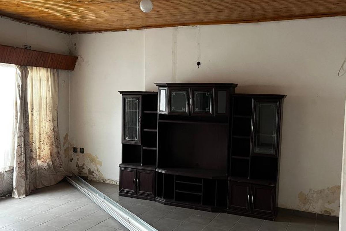 Living room featuring tiled flooring and a timber ceiling, currently requiring significant wall and ceiling repairs and cosmetic updates.