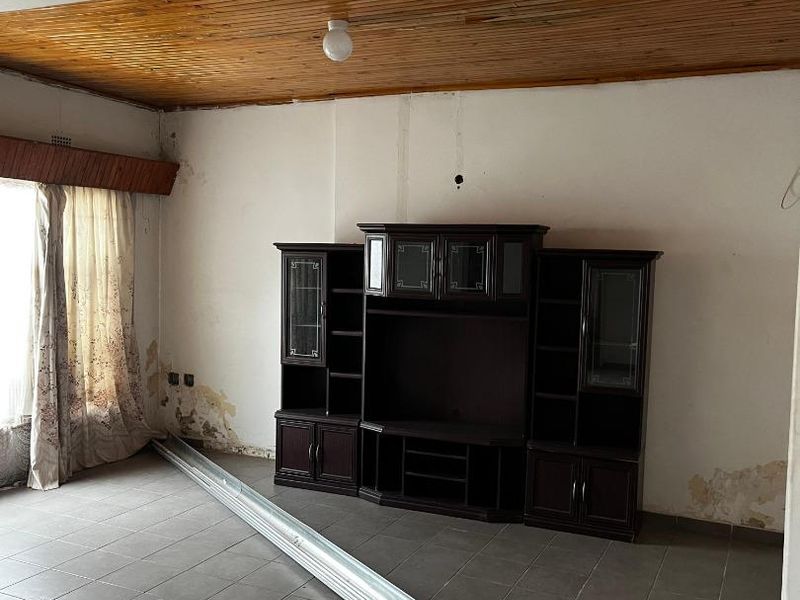 Living room featuring tiled flooring and a timber ceiling, currently requiring significant wall and ceiling repairs and cosmetic updates.