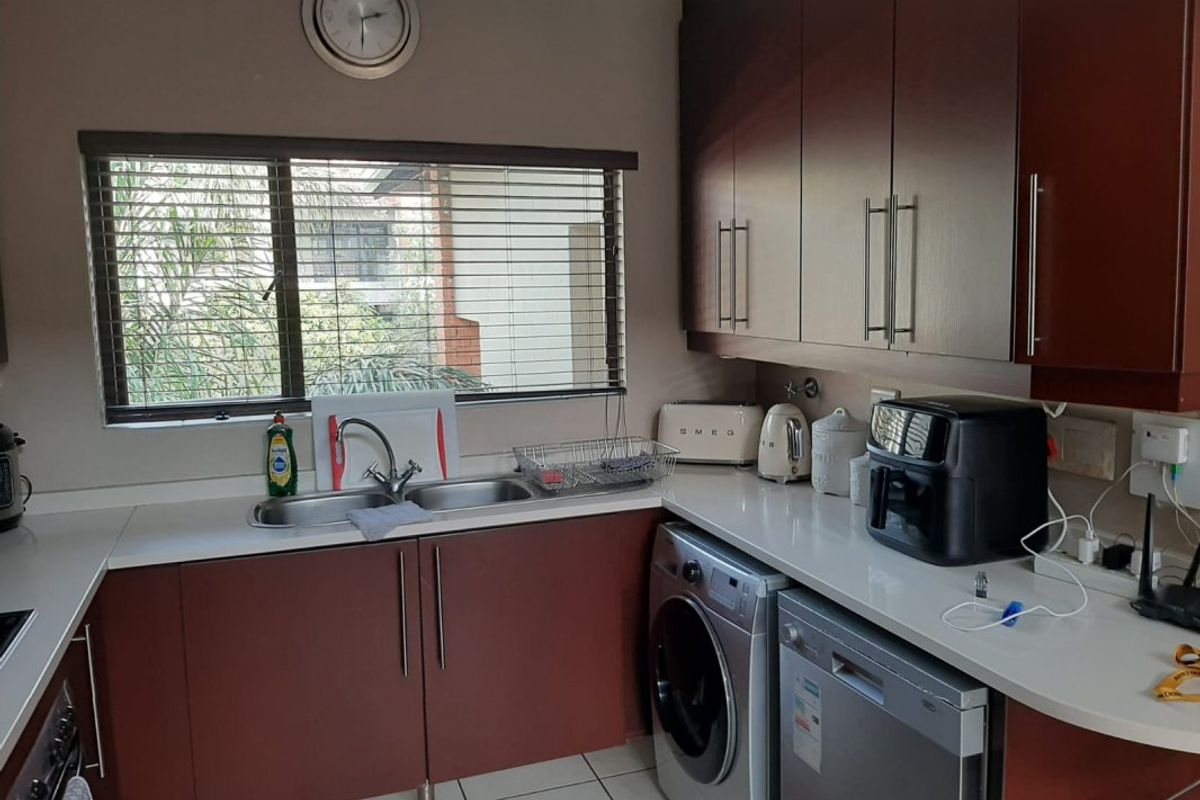 A functional kitchen featuring dark wood cabinetry, white stone countertops, a double basin sink, and integrated laundry and dishwasher appliances.