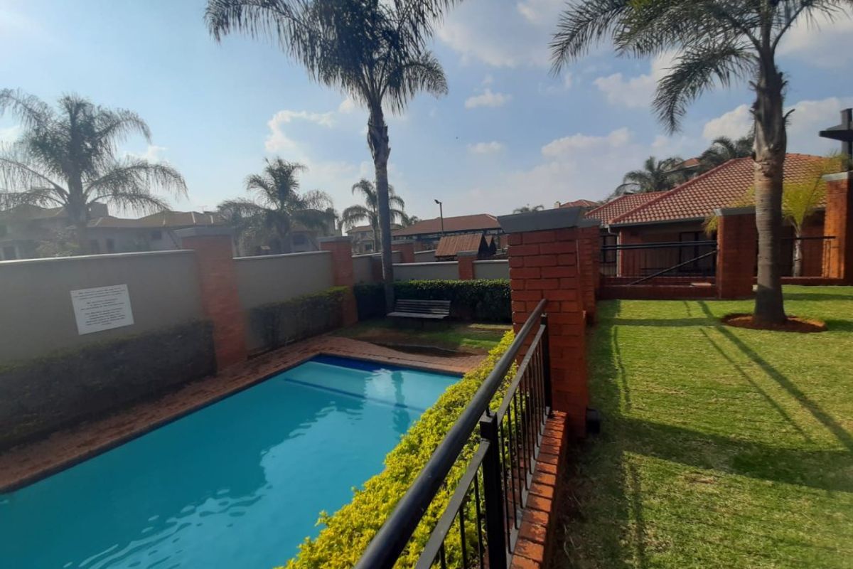 A well-maintained outdoor pool area featuring a swimming pool, manicured lawn, and brick boundary walls with metal safety railings.