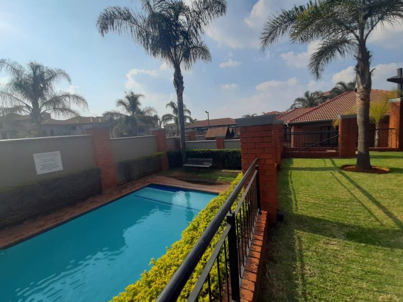 A well-maintained outdoor pool area featuring a swimming pool, manicured lawn, and brick boundary walls with metal safety railings.