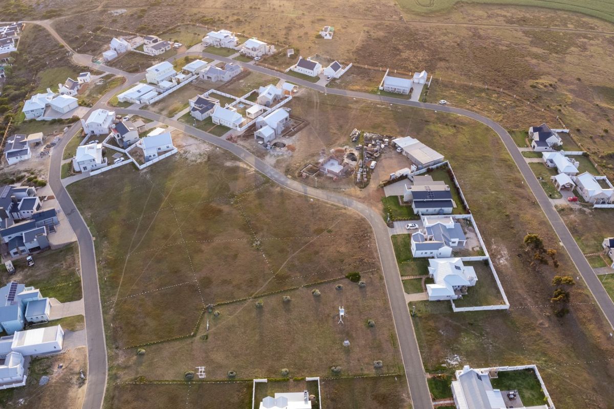 An aerial view of a residential estate featuring developed housing plots, paved road infrastructure, and surrounding open land.