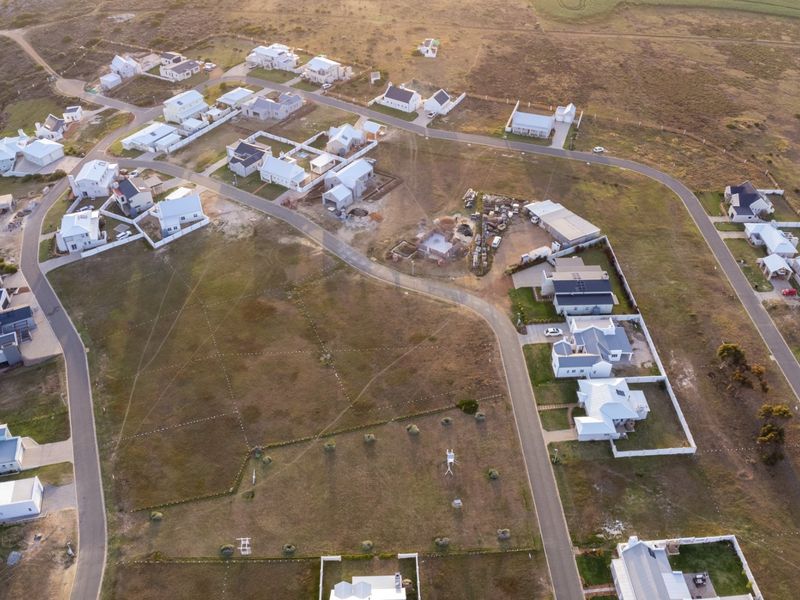 An aerial view of a residential estate featuring developed housing plots, paved road infrastructure, and surrounding open land.