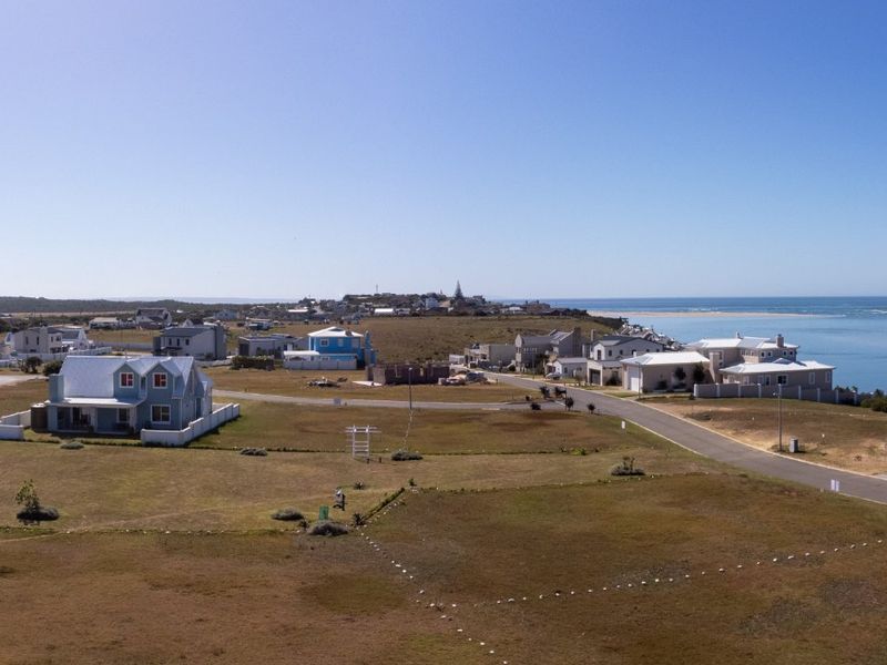 An aerial view of a coastal residential estate featuring vacant land plots, established homes, and proximity to the ocean.
