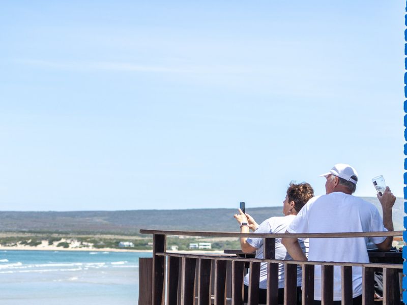 A scenic coastal view captured from a raised deck featuring a wooden balustrade and blue brick pillar.