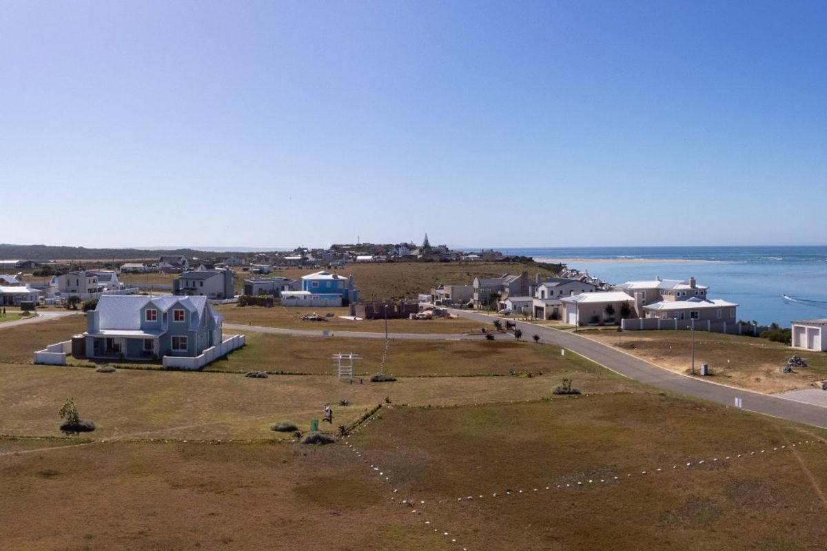 An aerial view of a coastal residential estate featuring vacant land plots, established homes, and proximity to the ocean.