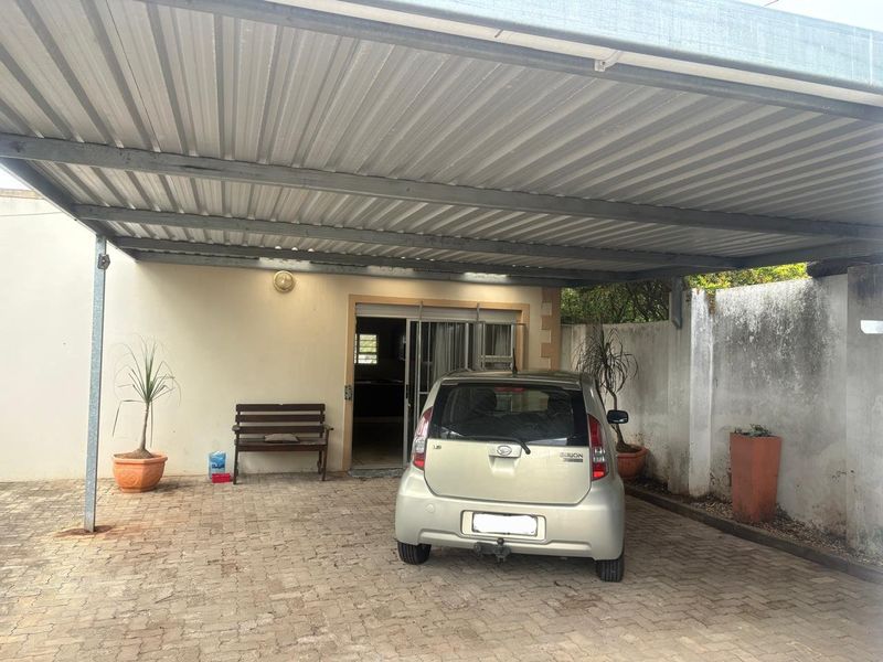 Covered carport area with paved flooring and direct access to the apartment through a sliding glass door.