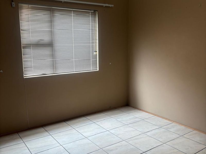 An empty bedroom featuring neutral wall paint, tiled flooring, and fitted venetian blinds.
