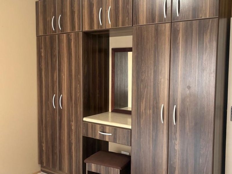 A bedroom featuring a large, dark wood-grain built-in wardrobe with an integrated vanity station and tiled flooring.