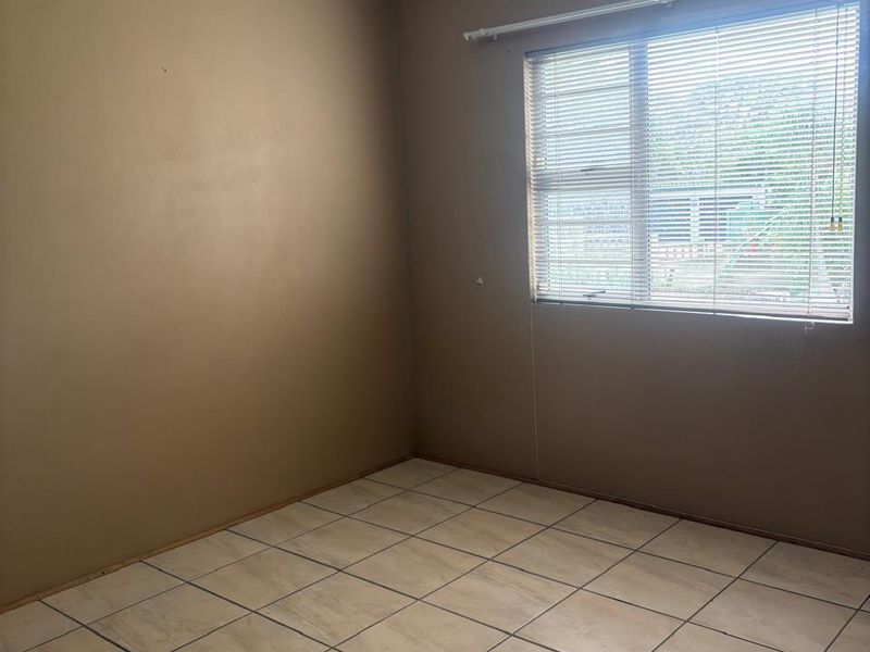 An empty bedroom featuring neutral wall paint, tiled flooring, and fitted venetian blinds, offering a blank canvas for personalization.