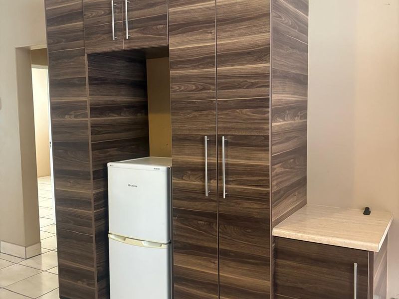 A kitchen area featuring dark wood-grain built-in cabinetry, a light laminate countertop, and tiled flooring.