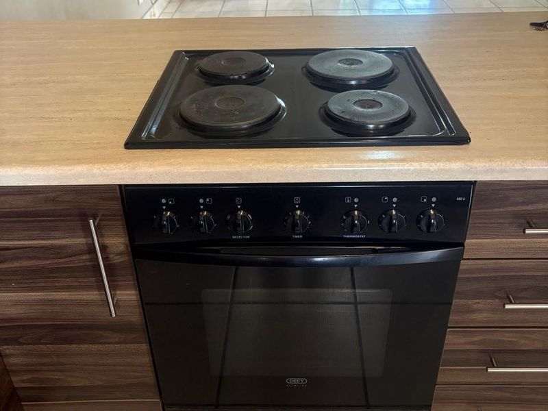 A functional kitchen area featuring a built-in Defy oven and electric hob set into a laminate countertop with dark wood-finish cabinetry.