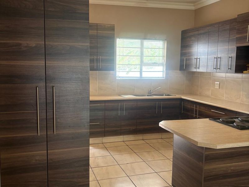 A clean, functional kitchen featuring dark wood-grain cabinetry, laminate countertops, a built-in hob, and neutral tiled flooring throughout.