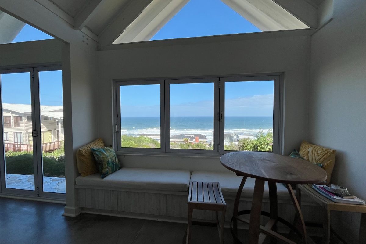 Bright living area featuring a vaulted ceiling, exposed rafters, and a built-in window seat offering expansive ocean views through large windows.