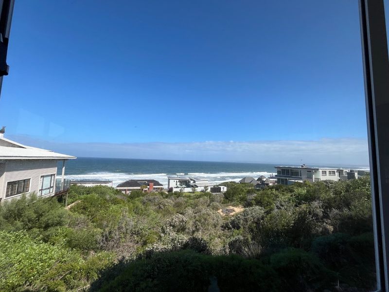 A scenic elevated view overlooking coastal vegetation and the ocean, captured from an interior vantage point.