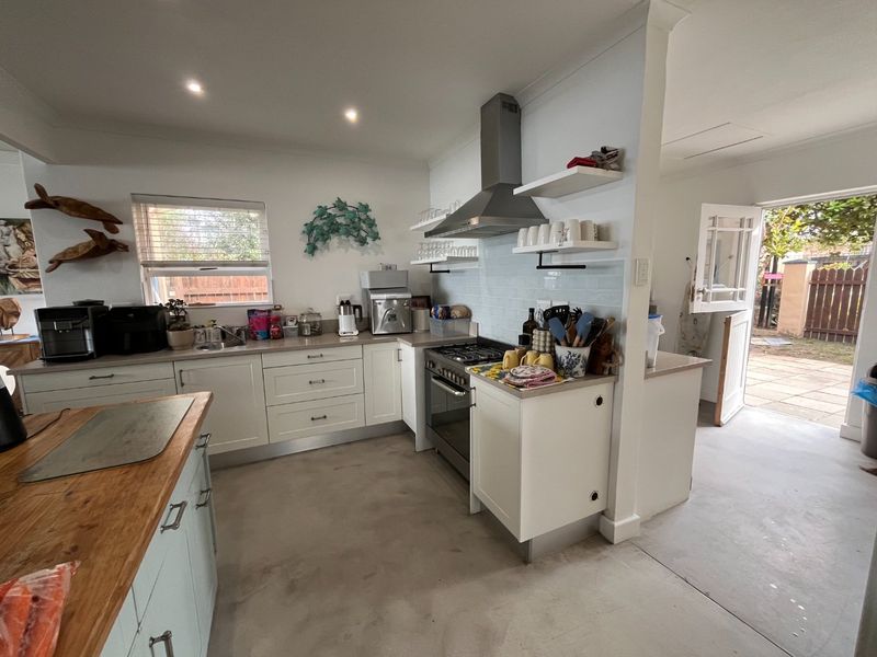 A functional kitchen featuring shaker-style cabinetry, a gas cooktop with stainless steel extractor, subway tile backsplash, and direct access to the rear patio.