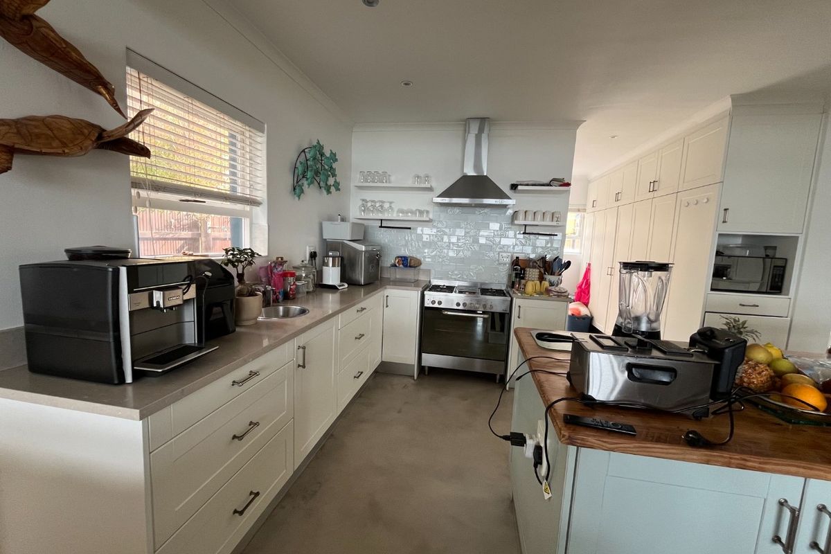 Modern kitchen featuring white cabinetry, stone countertops, a central island, stainless steel appliances, and a tiled backsplash with ample storage space.