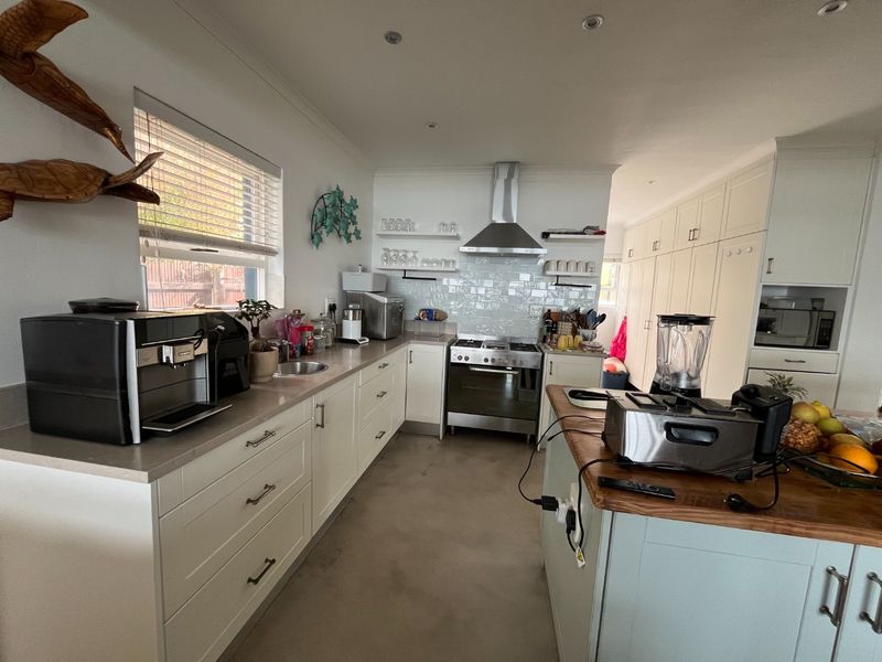 Modern kitchen featuring white cabinetry, stone countertops, a central island, stainless steel appliances, and a tiled backsplash with ample storage space.