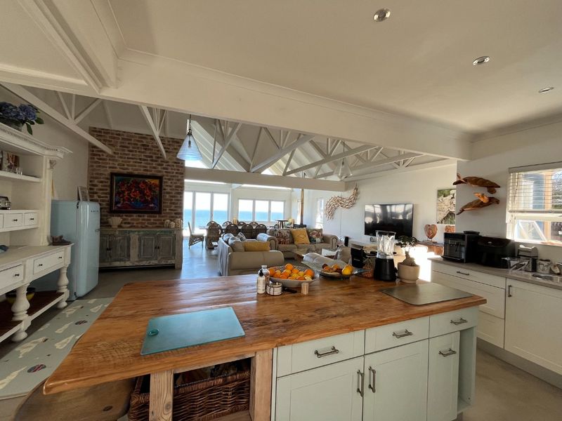 Spacious open-plan living area featuring exposed roof trusses, a large kitchen island, and an exposed brick wall with direct views of the ocean.