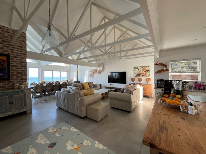 Spacious open-plan living area featuring vaulted ceilings with exposed trusses, polished concrete floors, an exposed brick fireplace, and a modern kitchen island.