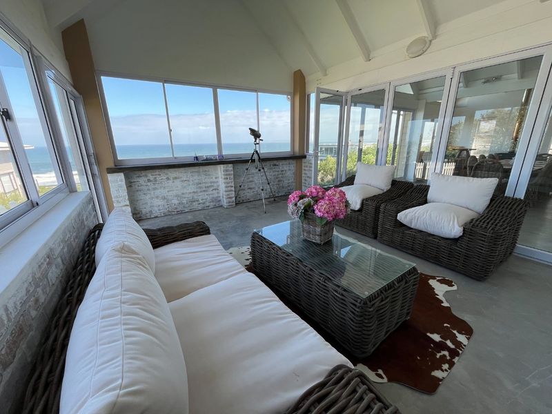 A bright, enclosed patio featuring a vaulted ceiling, exposed brick accents, and expansive windows offering panoramic ocean views.