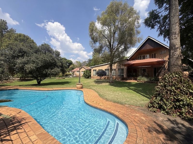 A spacious backyard featuring a swimming pool with brick coping, a well-maintained lawn, and a covered patio area attached to the main house.