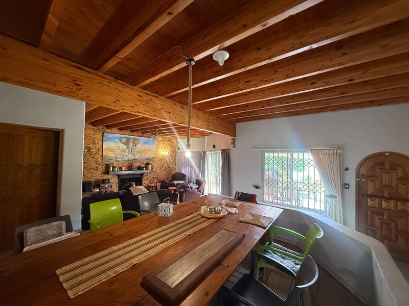 Open plan living and dining area featuring exposed timber beam ceilings, a fireplace with cork wall cladding, and tiled flooring.
