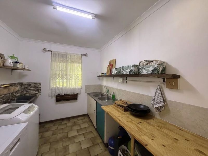 Functional laundry room featuring a double stainless steel sink, timber countertop, built-in cabinetry, and floating shelving with tiled splashback.
