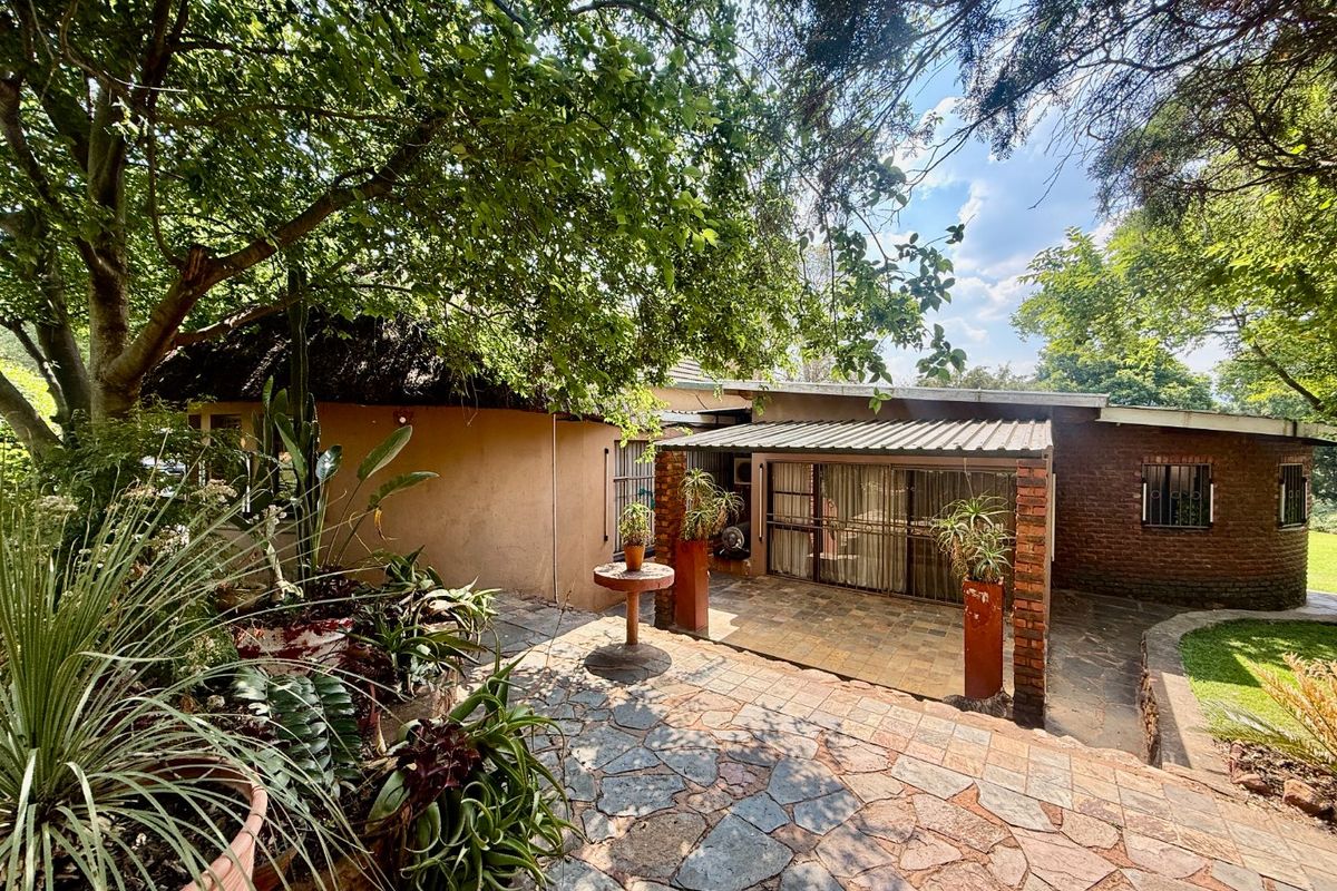 A rear exterior view featuring a stone-paved patio area with a covered section, brick pillars, and mature garden surroundings.