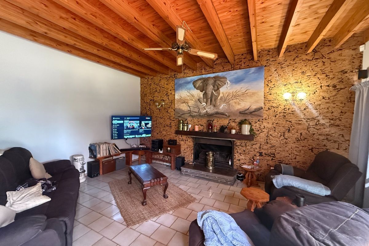Cozy living room featuring a distinctive cork feature wall, a built-in fireplace, and an exposed timber beam ceiling with a ceiling fan.