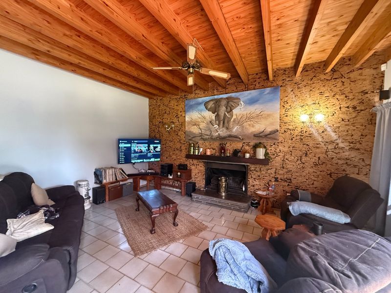 Cozy living room featuring a distinctive cork feature wall, a built-in fireplace, and an exposed timber beam ceiling with a ceiling fan.