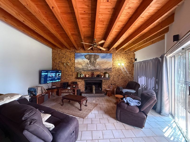 Spacious living room featuring a distinctive exposed timber beam ceiling, cork-clad feature wall, built-in fireplace, and direct access to the outdoors via sliding glass doors.
