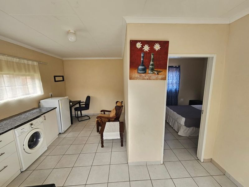 Open-plan living area featuring tiled flooring and a functional kitchen space with built-in cabinetry, leading directly into an adjacent bedroom.