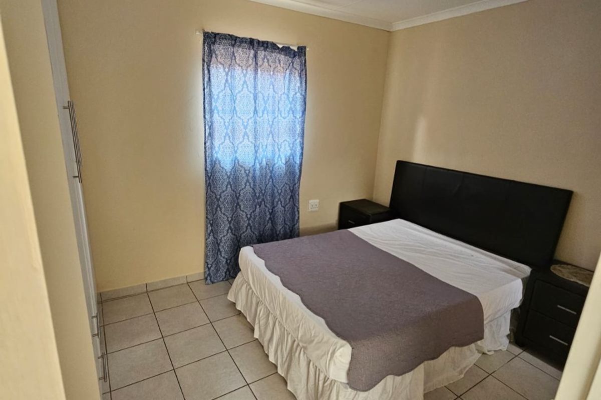 A functional bedroom featuring tiled flooring, a built-in wardrobe, and neutral wall finishes, providing a clean and simple living space.